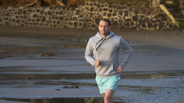 Slow motion shot of young caucasian man running on the beach in Auckland, New Zealand