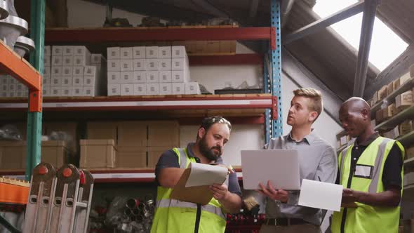 Two Caucasian and an African American male factory worker at a factory pointing, holding a clipboard