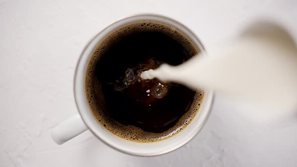 Adding Cream to a Cup with Black Hot Coffee Placed on White Table