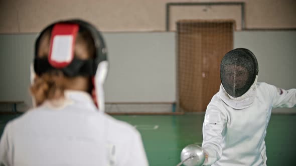 Two Young Women in Protective Costumes at Fencing Training in the School Gym - Standing in the