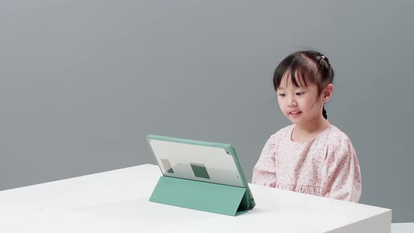 Child using digital tablet sitting near the table to watch cartoon. Record held in studio with gray