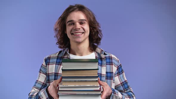 Student Holds Stack of University Books From Library on Violet Background in Studio