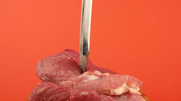 A large knife is stuck into a piece of red meat on a bright orange background.