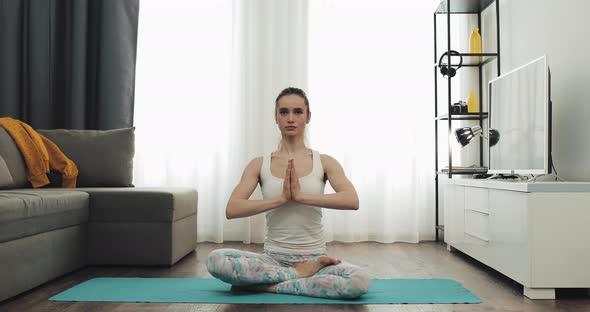 Portrait of a Young Woman Practicing Yoga Sitting on a Mat in Lotus Pose at Home.