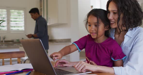 Happy hispanic mother and daughter sitting at table looking at laptop