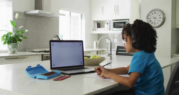 Happy biracial boy sitting at table using laptop with copy space and having online classes