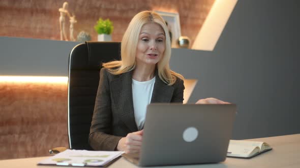 Friendly Caucasian Mature Elegant Woman Top Manager Ceo Sit in Office Using Laptop Talking By Video