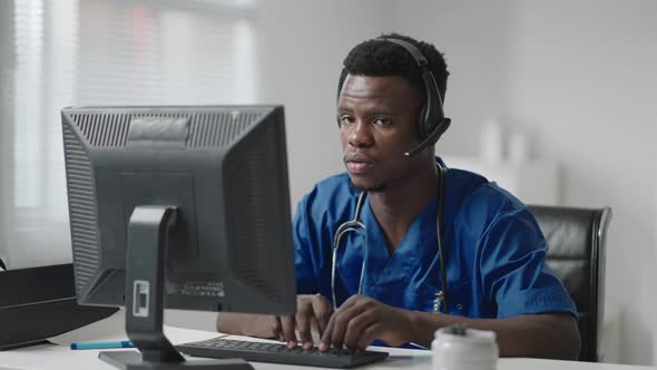 Afroamerican Male Doctor or Nurse with Headset and Computer Working at Hospital  alt