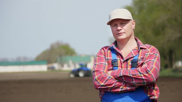 Portrait of Farmer or Agronomist, in Red Plaid Shirt, Against Background of Working Tractor