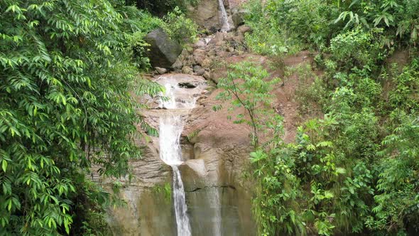 Aerial view of a tropical waterfall starting close to the water and zooming out to reveal waterfall