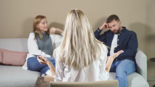 Rear View on Blond Young Psychologist Woman Looking at Quarrelled Couple Sitting Opposite