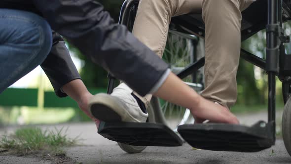 Unrecognizable Woman Adjusting Legs of Disabled Child on Wheelchair Legrest in Slow Motion