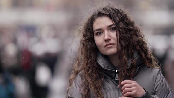 Portrait of a Young Woman with Curly Hair Walking on a City Street on a Cold Winter Day