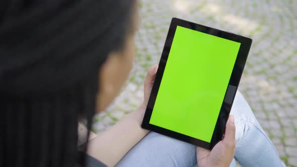 A Black Woman Looks at a Tablet with Green Screen - Vertical Position - Focused Closeup From Behind