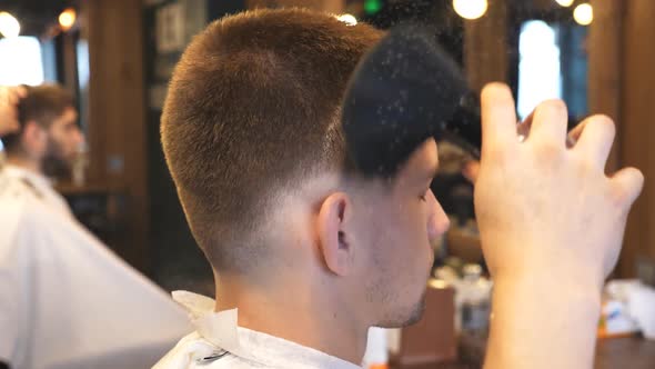 Male Barber Using a Talc for Young Client in Salon. Hairdresser Uses Brush To Clean Guy of Cutted