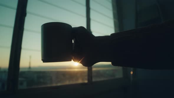 Silhouette of boy drinks tea at the window