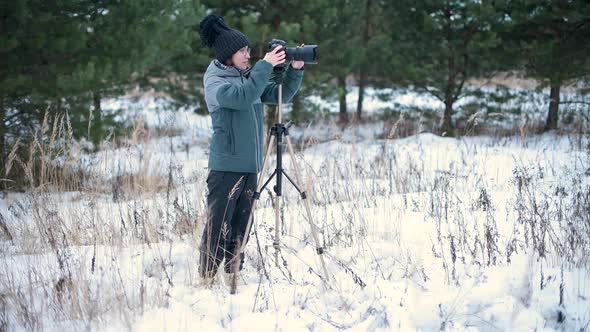 The girl enthusiastically takes pictures in the winter forest on a photo camera