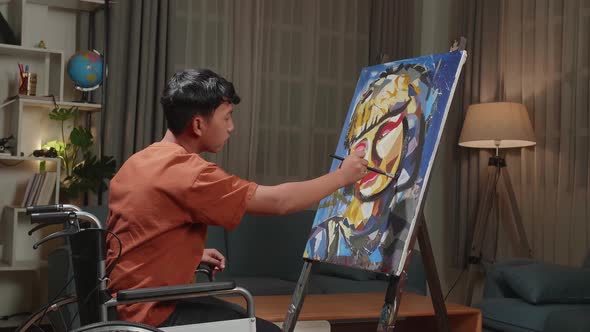 Asian Artist Boy In Wheelchair Holding Paintbrush Painting A Girl's Face On The Canvas