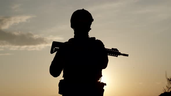 Silhouette of Military Man in Special Equipment with Sniper Rifle Against Background of Sunset