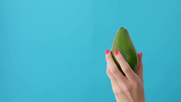 Avocado in a Hand of Woman Blue Background