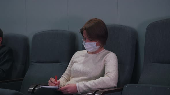 a Woman in a Mask Makes Notes in a Notebook
