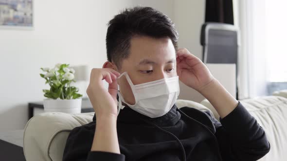 A Young Asian Man Takes Off His Face Mask, Breathes Out Sigh of Relief and Smiles Tiredly at Camera