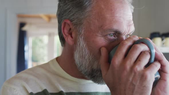 Caucasian mature man looking through the window and drinking coffee