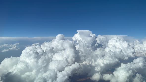 Stunning pilot view from a jet cockpit avoiding stormy cumulus clouds in a messy and deep blue sky