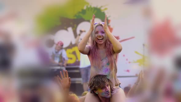 Smiling Young Woman Covered in Colorful Paint Sitting on Friends Shoulders