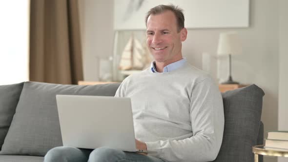 Middle Aged Businessman Doing Video Chat on Laptop on Sofa