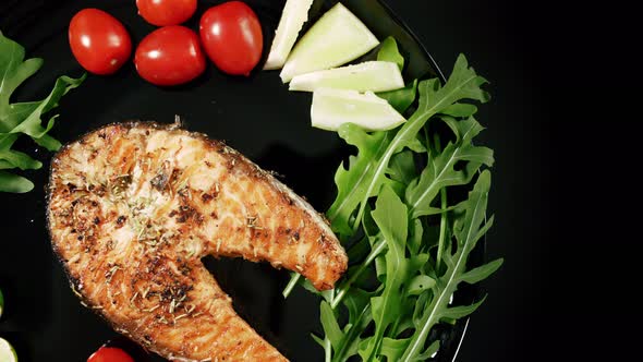 A Cooked Salmon Steak with the Addition of Aromatic Spices and Vegetables on a Black Serving Plate