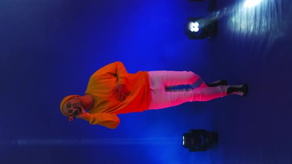 Vertical Video. A Man in a Yellow Jacket Dancing on a Blue Background. Singer in the Studio in Neon
