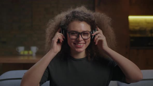 20s Young Woman in Eye Glasses Enjoys Listening Music in Wireless Headphones with Closed Eyes