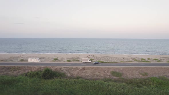 Drone Flying Near Tourist Car Driving Down Empty Coastal Road Near Sandy Beach