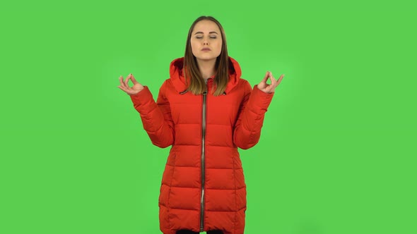 Lovely Girl in a Red Down Jacket Is Relaxing, Meditating at Studio. Green Screen