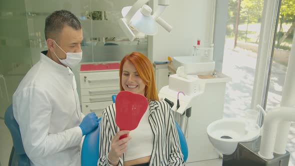 Professional Caucasian Male Dentist Show Beautiful Teeth in Mirror To Happy Woman Visitor. Positive