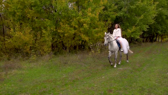 Long-haired Fiancee in White Dress Is Riding Horse Along Wood