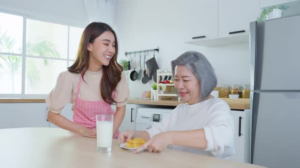 Asian lovely family, young daughter prepare breakfast for older mother in kitchen at house.