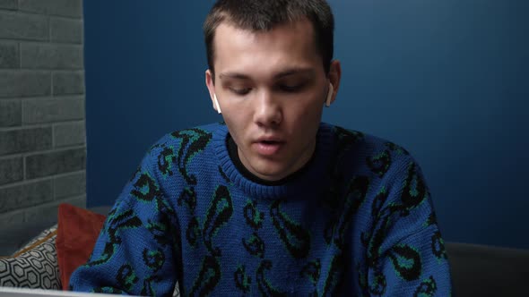 A Focused Handsome Young Caucasian Man Wearing Headphones Working and Using His Laptop on Sofa at