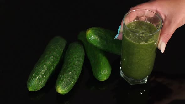 Girl Puts the Glass with Cucumber Smoothies on the Table with Black's Surface