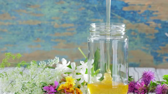A Stream of Fresh Honey Flows Down in Glass Jar on the Rustic Background