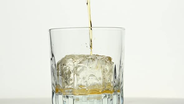 Pouring whiskey on ice rock in glass over white