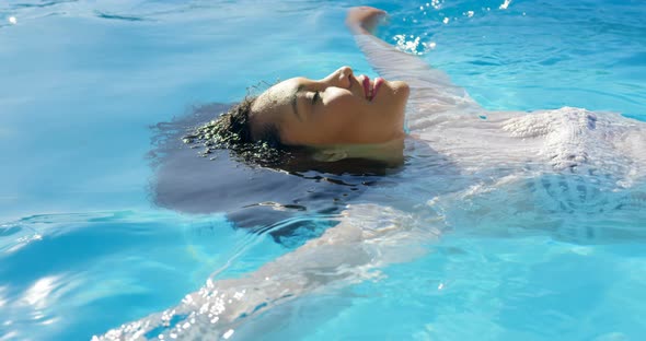 Side view of young mixed-race woman floating in swimming pool on a sunny day 4k