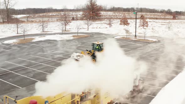 Snow plow tractor holding snow in bucket driving to a snow melter machine