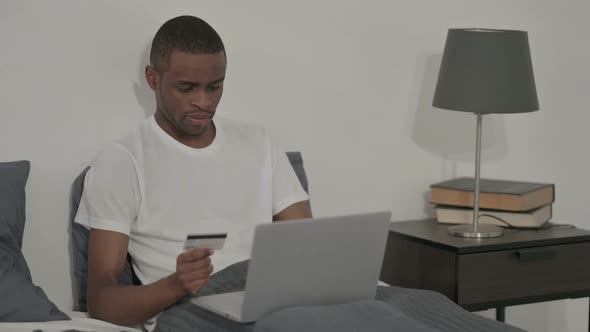 African Man with Successful Online Payment on Laptop Sitting in Bed