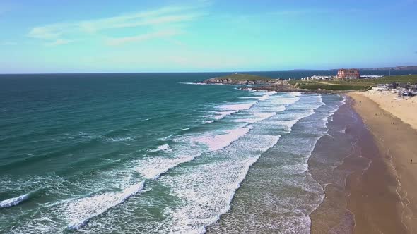 Wide drone shot of surfers waiting on waves as they break onto Fistral beach