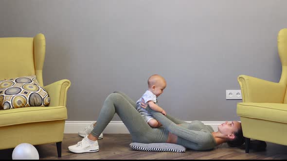 Young Slim Caucasian Mother Doing Sport Fitness Exercises Home with Baby Infant