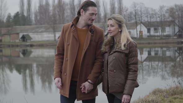 Portrait of Happy Man Walking with Loving Woman Along River or Lake and Kissing Her Hand. Positive