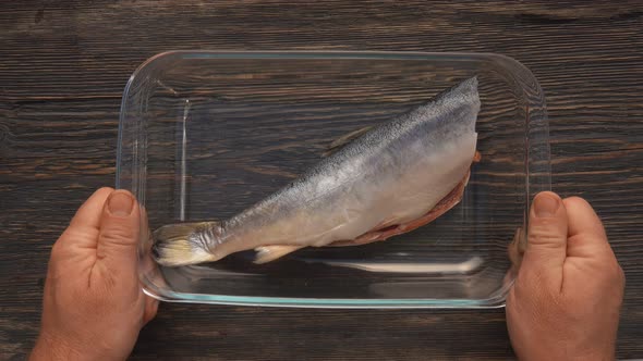 Top View of Hands Placing a Glass Tray with a Red Char Fish on the Wooden Table