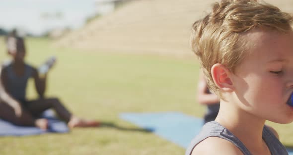 Video of focused diverse boys drinking water during exercising on mats on sunny day